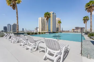 a row of white chairs sitting next to a swimming pool at Holiday Studio In JVC 2302, Dubai in Dubai