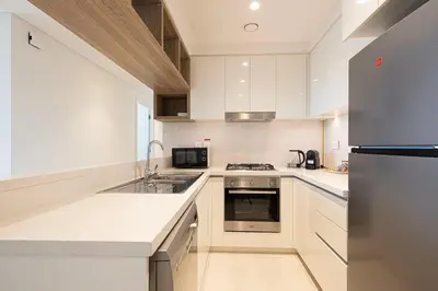 a kitchen with white cabinets and a stainless steel refrigerator at Burj Khalifa View, 2 Balcony w Lounge, Dubai Mall Access, Gym, Infinity-Pool, Playground, BBQ, Family Friendly in Dubai
