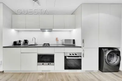 a kitchen with white cabinets and a washer and dryer at Belgravia Square, Jumeirah Village Circle in Dubai