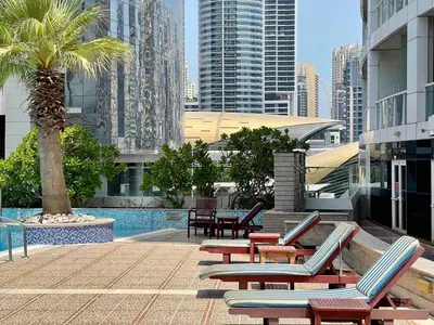 a pool with lounge chairs and a palm tree and buildings at Rustic Elegance By The Lake Studio Cabin In Jlt in Dubai