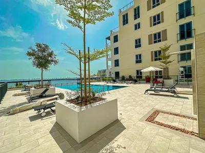 a building with a pool and two trees in a courtyard at HiGuests - Coastal Chic Luxurious Retreat at Port de la Mer in Dubai