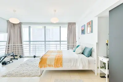 a white bedroom with a bed and a large window at Jlt Spacious Corner Duplex Loft Panoramic Views in Dubai