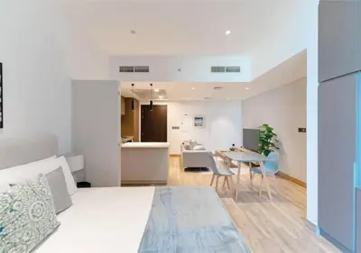 a bedroom with a bed and a table and a kitchen at HAVN - Studio Apartment in Chaimaa Avenue, JVC in Dubai