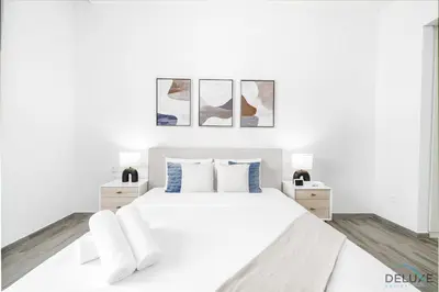 a white bedroom with a white bed and three pictures on the wall at Lovely 2BR at Belgravia Square, JVC by Deluxe Holiday Homes in Dubai
