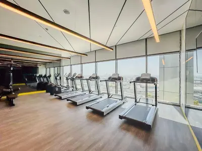 a gym with a row of treadmills and windows at High-Floor 2BR in Aykon City Spacious, Good View in Dubai