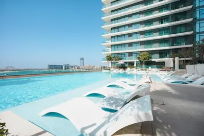 a swimming pool with white chairs and a building at Stayis I Beachfront Luxury 1BR with Private Access in Dubai
