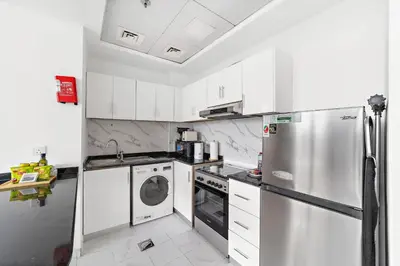 a kitchen with white cabinets and a stainless steel refrigerator at Silkhaus Chic Luxury Studio Opposite Silicon Oasis Shopping Mall in Dubai
