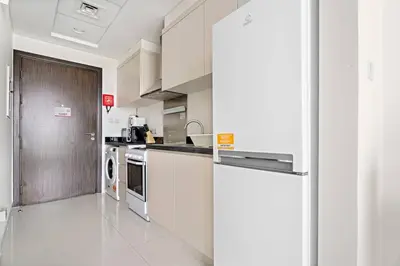 a kitchen with white cabinets and a refrigerator at Cozy Studio in Damac Hills in Dubai