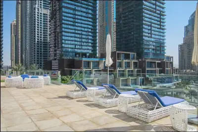 a row of chairs and umbrellas on a patio with tall buildings at Cayan Tower Dubai Marina - By Home Of Choice in Dubai