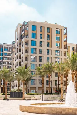 a building with palm trees in front of a fountain at SettlerHomes - Marvelous Lagoon Stay With Pool View in Dubai