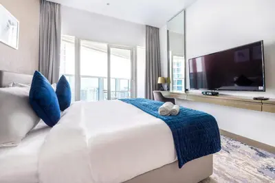 a large white bed with blue pillows and a tv at Studio Apartment in DAMAC Maison Prive Businessbay - Dubai Canal View in Dubai