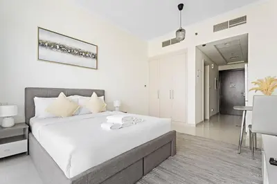 a white bedroom with a large bed and a table at Comfortable Studio in Damac Hills in Dubai