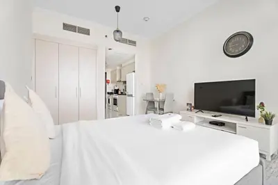 a white bedroom with a large bed and a tv at Cozy Studio in Damac Hills in Dubai
