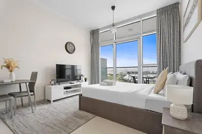 a bedroom with a bed and a desk and a large window at Cozy Studio in Damac Hills in Dubai