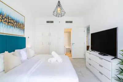 a white bedroom with a large bed and a flat screen tv at Stylish 1BR Apartment with City View Balcony Pool and Parking in Dubai