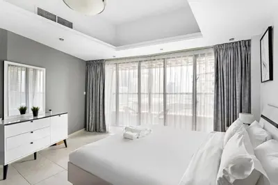 a white bedroom with a large bed and large windows at Stylish Studio in Prime Location in Dubai