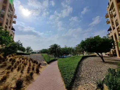 a walkway through a park with trees and buildings at YALLA REMRAAM in Dubai
