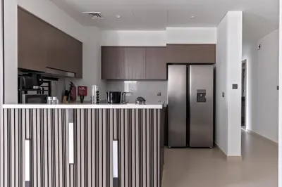 a kitchen with a stainless steel refrigerator and wooden cabinets at Luxurious 4BR Apartment w/ Prime Burj Khalifa View in Dubai