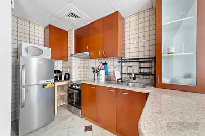 a kitchen with wooden cabinets and a stainless steel refrigerator at WelHome - Stylish Studio with Park Views in Regent House 2 in Dubai