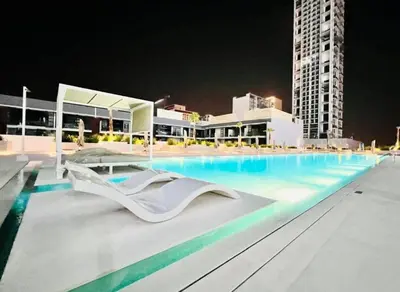 a large swimming pool with chairs and a building at Luxe 1BR 15mins-Beach Best Infinity Pool -Jumeirah Village Circle, JVC ,Dubai in Dubai