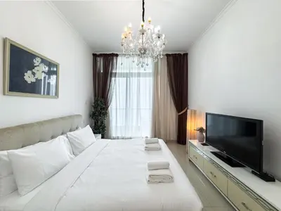 a white bedroom with a large bed and a television at SettlerHomes- Breathtaking 2BR Marina High-Floor in Dubai