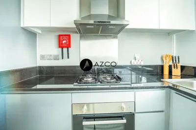 a kitchen with white cabinets and a stove top oven at Panoramic 2BR - 3 Balconies & Canal Views - Damac Maison Prive by AZCO Holiday Homes in Dubai