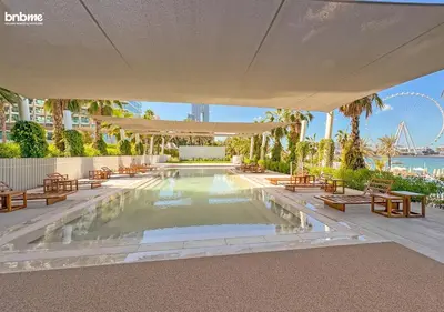 a swimming pool with tables and a large umbrella at bnbme - Luxury 1BR La Vie Apt Beach Access Pool Gym Balcony & Stunning Dubai Eye Views in Dubai