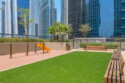 a park with benches and grass in front of tall buildings at Frank Porter - Zada Tower in Dubai