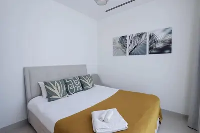 a white bedroom with a bed with a gold blanket and a white towel at Stylish 2 bedroom apartment in Sobha Hartland in Dubai