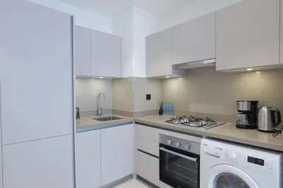 a kitchen with white cabinets and a washer and dryer at Stylish 2 bedroom apartment in Sobha Hartland in Dubai