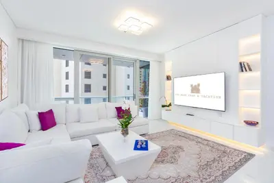a white living room with a white couch and a tv at High class apartment in Dubai