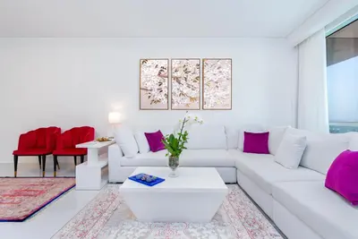 a white living room with a white couch and pink pillows at High class apartment in Dubai