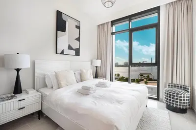 a white bedroom with a large bed and a window at Bright 2BR with Pool & Creek Views in Dubai