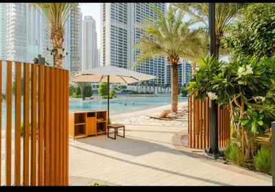a table with an umbrella next to a pool with buildings at Exquisite 1-Bedroom with Pool Scenery in Dubai Creek Harbour in Dubai