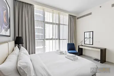 a bedroom with a white bed and a blue chair at WelHome - Charming Breathtaking 1BR Apt. In Damac Hills in Dubai