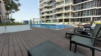 a swimming pool with chairs and a building at WelHome - Charming Breathtaking 1BR Apt. In Damac Hills in Dubai