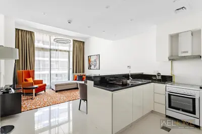 a kitchen with white cabinets and a living room at WelHome - Charming Breathtaking 1BR Apt. In Damac Hills in Dubai