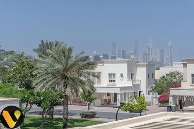 a building with a palm tree in front of a city at Vogue Springs Emirates Living near The Springs Souk, JBR, Marina, Mall of the Emirates, Spacious Villa with Garden and access to Lake and all Amenities in the Community in Dubai