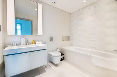 a white bathroom with a tub and a toilet and a sink at Elegant 1BR Apartment with Free Beach Access in Dubai