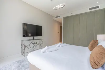 a white bedroom with a large bed with a television at Serene and sophisticated Lagoon Living - Suiteable in Dubai