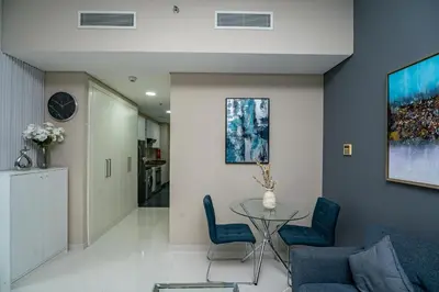 a living room with a glass table and blue chairs at Escape24 Studio at Loreto with Community View in Dubai