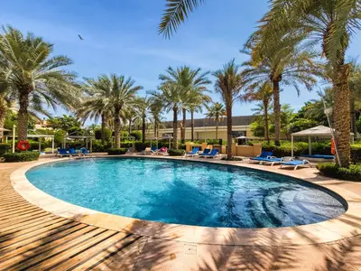 a swimming pool with palm trees and blue lounge chairs at Spacious 1BD apartment in the Residence North in Dubai