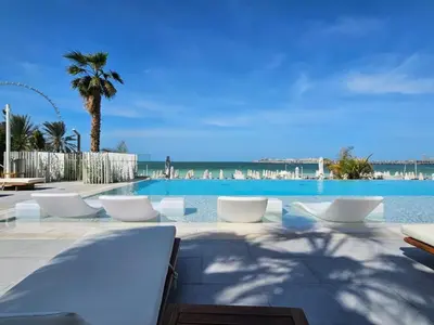 a pool with white chairs and a palm tree and the ocean at Beachfront Luxury Living at La Vie Residence JBR in Dubai