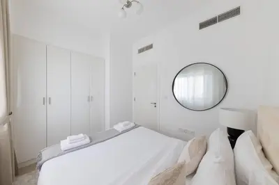 a white bedroom with a bed and a mirror at Comfortable 2BD apartment next to metro & mall in Dubai