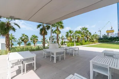 a patio with white tables and chairs and palm trees at Ahlan HH - Luxurious 1BR Suite at La Vie - Free Private Beach Access in Dubai
