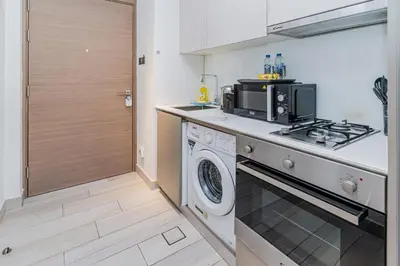 a kitchen with a stove top oven next to a washing machine at Elegant Studio Stay I Pool, Gym & Parking in Dubai