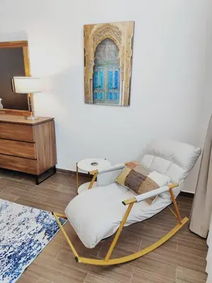 a rocking chair in a living room with a table at 1 Bed room - Azizi Daisy - Furjan in Dubai
