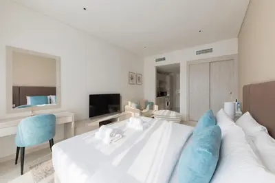 a white bedroom with a white bed and a blue chair at Chic Palm Studio with Infinity Pool in Dubai