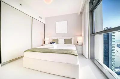 a white bedroom with a bed and a large window at Marina Vista 1BR Sea View Luxury Escape in Dubai