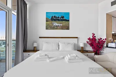 a white bedroom with a white bed and a window at WelHome - Relaxing and Fancy Studio Apt with City View in Dubai